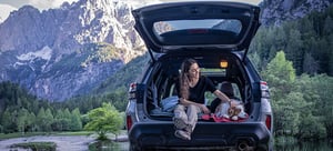 Frau sitzt mit liegendem Hund auf Kofferraumkante eines Subaru Forester