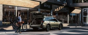 Subaru Outback mit geöffnetem Kofferraum wird mit Fahrrad beladen.